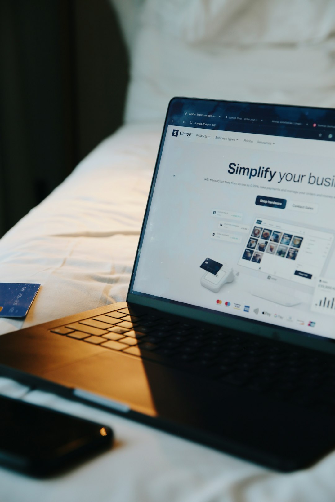 our-story Laptop displaying the SumUp website on a bed, with soft natural light and a credit card nearby. A visual representation of remote business management, online sales, and the flexibility of running a digital-first company from anywhere.